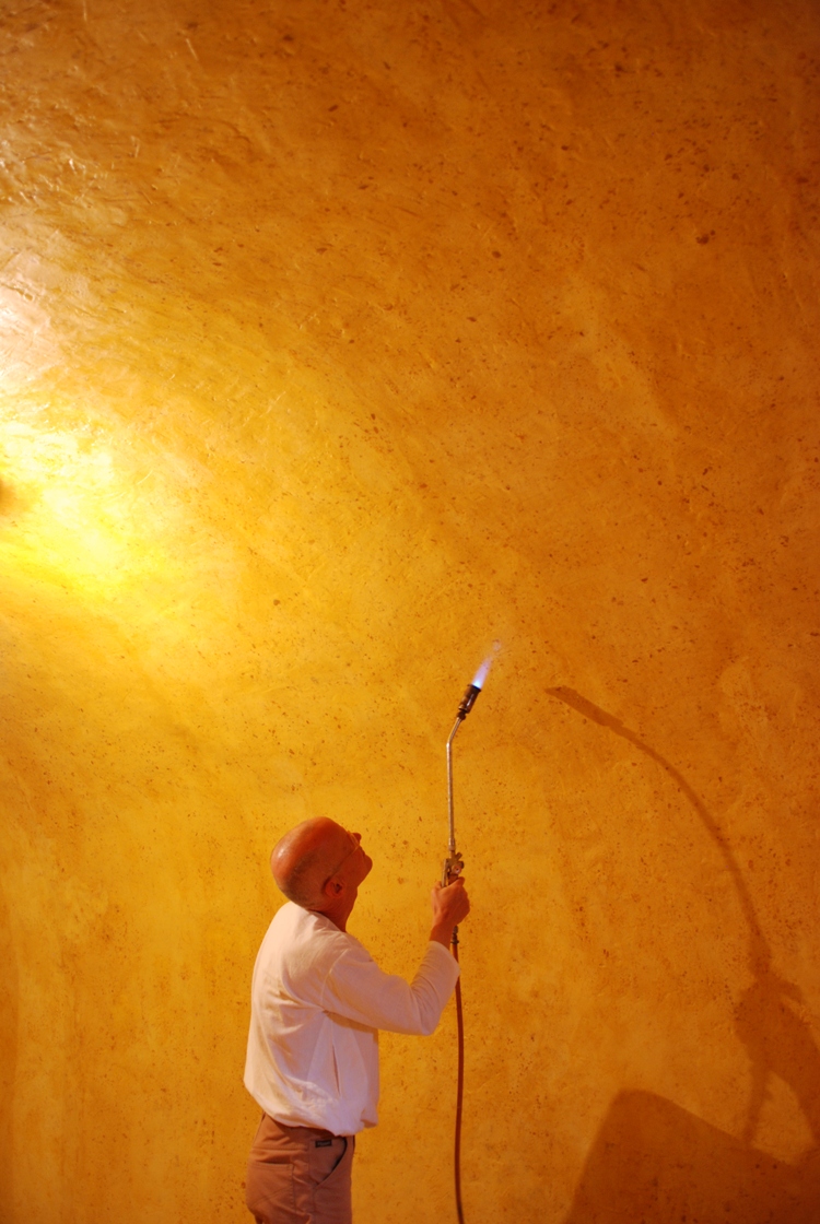 Wolfgang Laib finishes the walls of his wax rooms with a flame, which gives a unique shine to the beeswax surface. Here the artist works on a permanent wax chamber realized in a historic building in Switzerland.